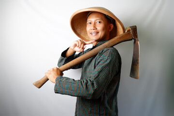 Happy Asian farmer wearing Lurik and Caping looking at camera. His right hand pointing to Cangkul isolated on white background. Human gestures concept - obrazy, fototapety, plakaty