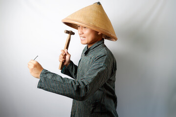 Indonesian farmer wearing Lurik and Caping hitting nail using a hammer isolated on white background.