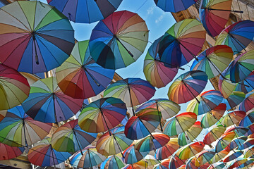 Bucharest, Romania: large group of rainbow coloured umbrellas suspended in the air in a narrow side...