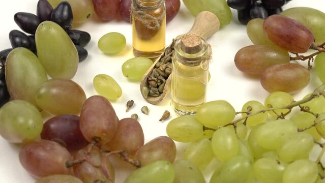Grapes and grape seeds, glass bottles with grape seed oil lie on a white table. Cosmetics based on grape oil