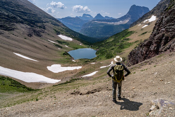 Mature Caucasian Man Hiker standing watching an alpine scene of a lake in a deep canyon surrounded by mountains, Ptarmigan Lake, Glacier National Park, Montana