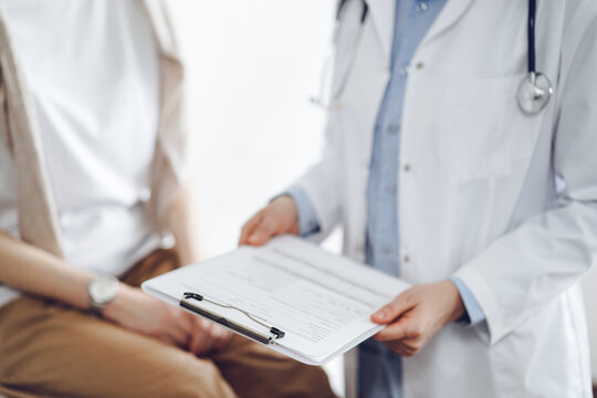Doctor and patient discussing perfect health exam results. Friendly physician keeping with hands clipboard with medical papers near young woman. Medicine concept