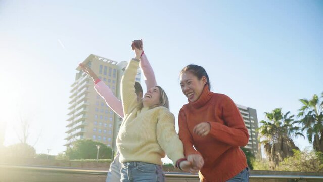 Three friends celebrate raised arms jumping, dancing and laughing outdoors having fun together. High quality 4k footage