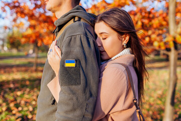 Close up of woman hugging husband in ukrainian military uniform with flag chevron from back. Sad...