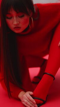 Asian girl with freckles on her face poses in front of the photographer on a red background in the pose of a cat. model in heels. vertical video. geisha model