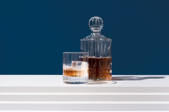 Vaso de whisky con hielo y decantador sobre fondo azul