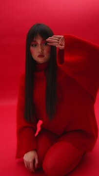 beautiful girl in red clothes on a red background sits and poses in front of the photographer. vertical video