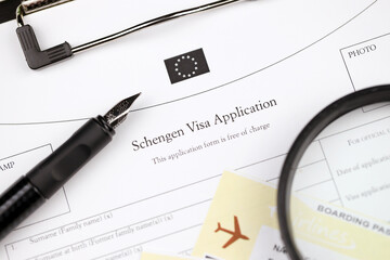 Schengen visa application on A4 tablet lies on office table with pen and magnifying glass close up