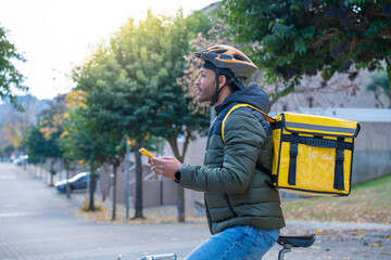 Delivery man on bike looking GPS location in the phone. Black courier delivering food and drink in...