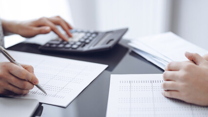 Woman accountant using a calculator and laptop computer while counting taxes for a client. Business audit concepts