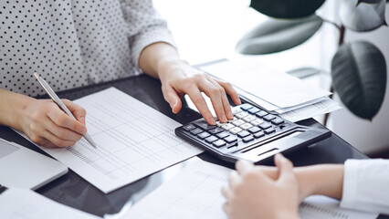 Woman accountant using a calculator and laptop computer while counting taxes with a client or a...