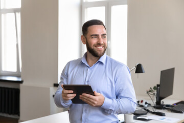 Happy successful millennial businessman holding digital tablet computer, looking away, thinking, planning, smiling , using gadget for wireless Internet connection, online app for job tasks