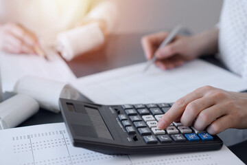 Two accountants use a calculator and laptop computer for counting taxes or revenue balance. Business, audit, and taxes concepts