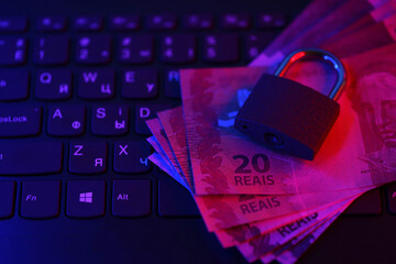 Closed padlock with brazilian reais money bills on laptop keyboard close up. Safe online banking or...