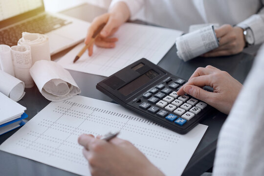 Two accountants use a calculator and laptop computer for counting taxes or revenue balance. Business, audit, and taxes concepts