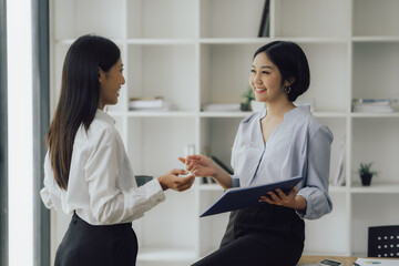 Two pretty young Asian businesswomen standing to discuss working on investment projects and...