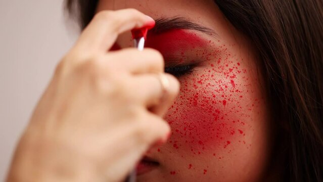close-up of asian girl with brown hair and cheekbones makeup artist splashing red drops on face on cheeks. art makeup
