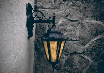 Closeup shot of an old-fashioned lantern on a white building against a stone wall