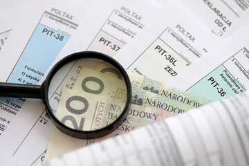 Polish zloty money and magnifying glass on big amount of polish tax forms close up. Accounting, bureaucracy and taxpayers routine in Poland