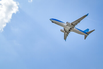 Fototapeta na wymiar Blue and white aircraft photographed from below shortly after take-off, flying towards a cloud in a blue sky