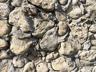 Fragment of a decorative textured wall made оf brown stones of different sizes and shapes and cement, close-up, front view. Fence. Parapet. Design. Construction.