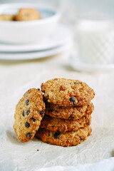a pile of oatmeal cookies and one cookie on the side next to it, close-up, a glass of milk behind, light background