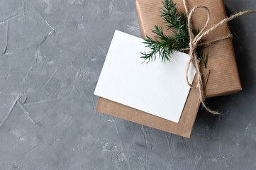 Christmas gift box with empty paper card and envelope on neutral gray table background....