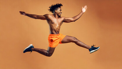Athletic man jumping in dynamic pose, dance, wearing orange shirt and pants, yellow background, studio portrait