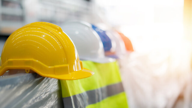 A row of safety helmets and vests are lined up. The helmets are yellow and the vests are bright orange and yellow. Concept of safety and caution, as the workers are wearing protective gear