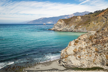 Turquoise water of northern California Pacific seacoast and coastal mountains with blue sky and clouds..