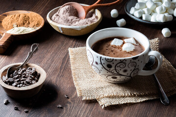 A cup of hot cocoa with mini marshmallows and cocoa ingredients all around.