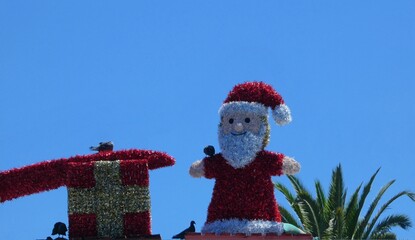 Low angle shot of a Santa Claus and gift figure made from tinsel with pigeons perched on it