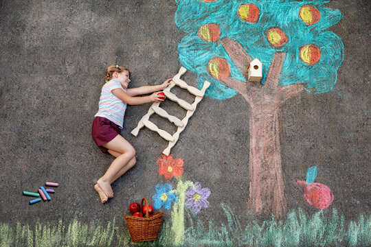 Cute little girl painting with colorful chalks apples harvest from apple tree on asphalt. Cute preschool child with having fun with chalk picture. Creative leisure for children, drawing and painting.