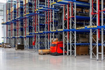 Hohes Hochregal mit wenigen Paketen in einer Industrie-Halle mit Intralogistik / Logistik mit rotem Stapler / VNA 