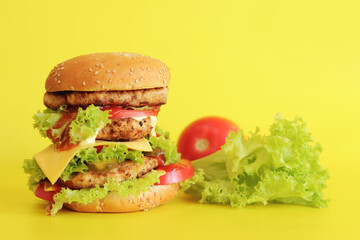Cheeseburger and fresh vegetables on a yellow background. Juicy tasty burger on a bright background, side view. Fast food