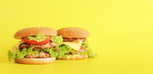 Two cheeseburgers on a yellow background. Juicy tasty burger on a bright background, side view. Fast food. Copy space