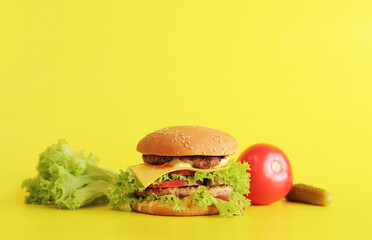Cheeseburger and fresh vegetables on a yellow background. Juicy tasty burger on a bright background, side view. Fast food