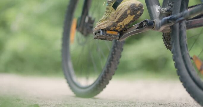Abstract mountainbiker getting ready to ride. Man riding a mountainbike on a dusty dirth road path. Closeup pedal shoe and gear shift. Recorded at 120 fps on cinema camera.