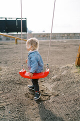 Little girl stands near a rope swing on the playground and looks away