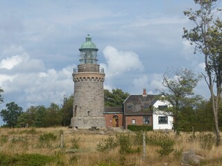 Fototapeta na wymiar Hammeren Lighthouse on Bornholm island surrounded by vegetation and with a cloudscape in background