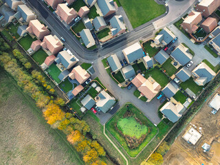 New housing estate seen during late autumn at the edge of an autumnal park. A large attenuation pond can be seen in the lower right, used for water drainage.