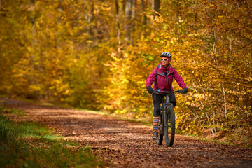 nice senior woman riding her electric mountainbike on the autumnal forest trails near...