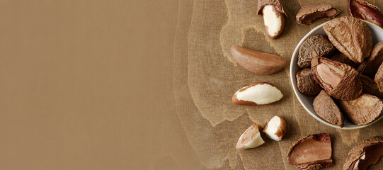 Unshelled and shelled Brazil nuts banner, brown table. Top view.
