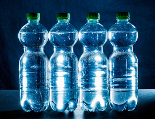 Four plastic bottles with water in front of a dark background
