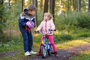 School kid boy, brother put on little preschool sister girl bike helmet on head. Brother teaching...