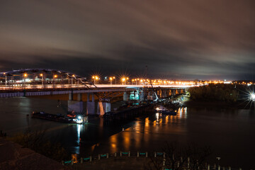 Night photo of a road bridge over a river, a cityscape, the light of street lamps on the road.