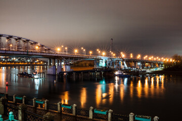 Night landscape of the city bridge over the river, lights of the evening city, the light of lanterns in the night.