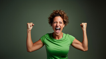 mujer de mediana edad mostrando músculos de brazos, fuerte, positiva, vestida de verde  - obrazy, fototapety, plakaty