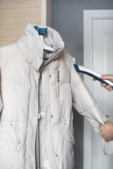 A man uses a steamer to steam a winter jacket, parka, or down jacket. © Mariya Surmacheva