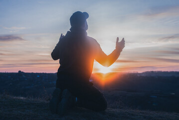 Prayer. Man on his knees praying. On the background of the sunset sky. Kneeling Prayer to God....